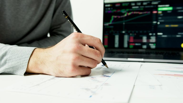 Close-up of a person analyzing financial charts with a laptop displaying stock market data.